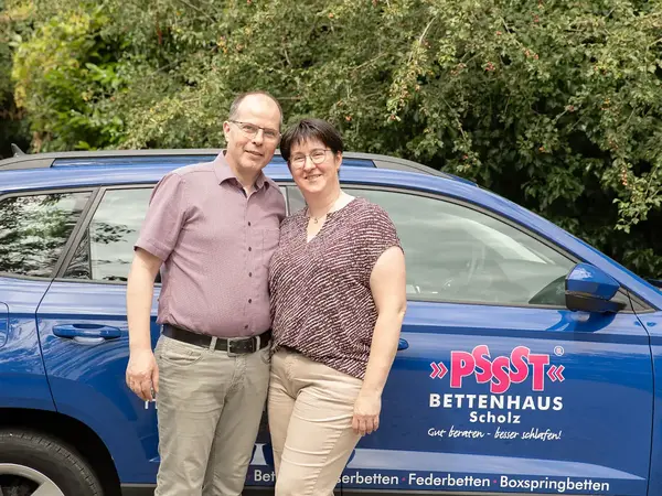 Paar vor blauem Firmenauto von Pssst Bettenhaus Scholz im Grünen